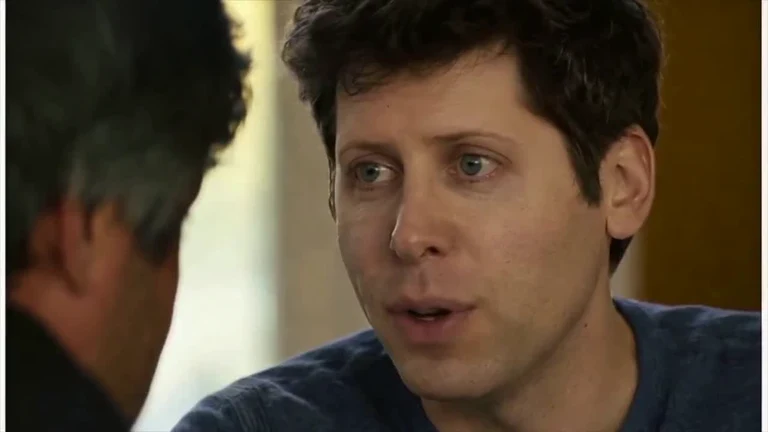 Close-up of a man with curly dark hair and green eyes showing a wide-eyed, open-mouthed surprised reaction during a conversation
