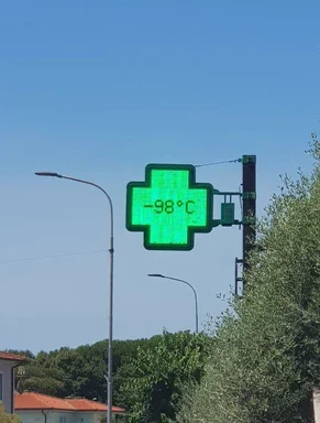 Green digital pharmacy cross sign displaying -98 degrees Celsius against a blue sky