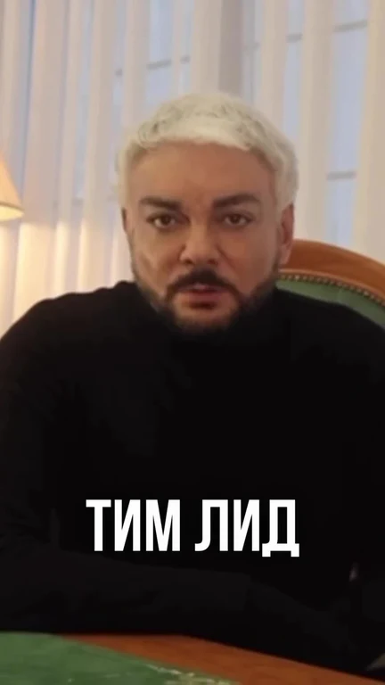 a man with white hair and a beard looks surprised or concerned, sitting at a table with a green top