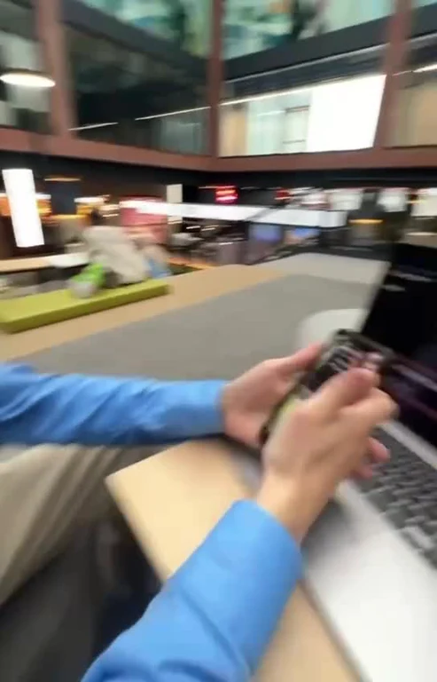 POV shot of a person holding a smartphone while sitting at a desk with a laptop in an office environment.