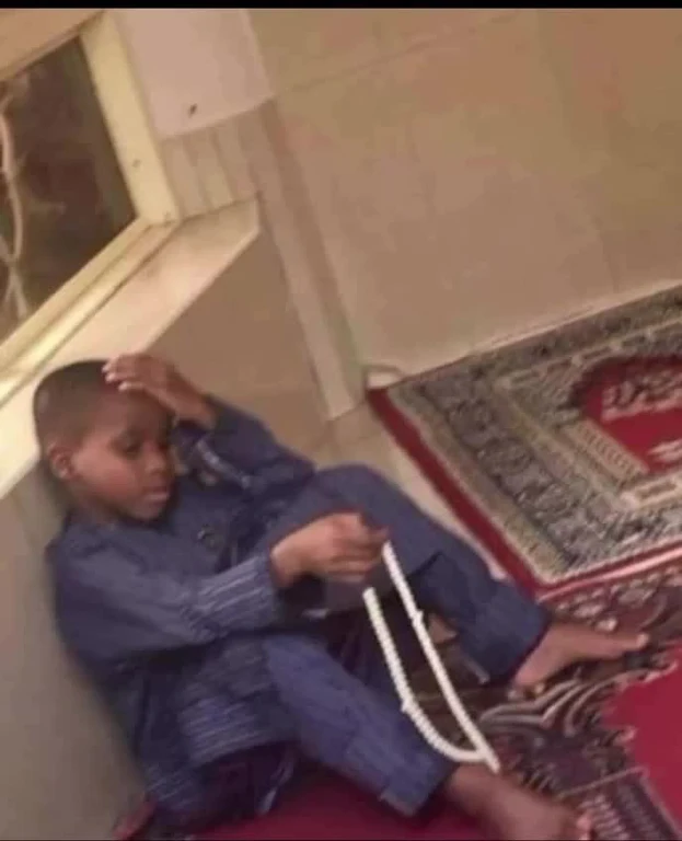 Young boy sitting on the floor looking stressed with hand on head and holding rosary beads