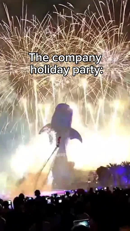 A whale-shaped firework exploding in the night sky above a crowd at a company holiday party