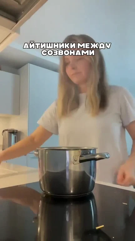 a woman in a white t-shirt standing in a kitchen with a pot on the stove