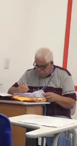 Older man with glasses sitting at a desk writing on a test paper