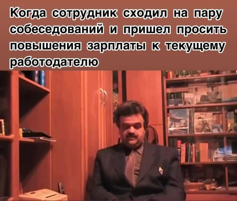 Man in a suit sitting in front of bookshelves with a serious expression