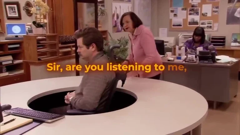 The Office scene with man sitting in desk hole with woman standing over him