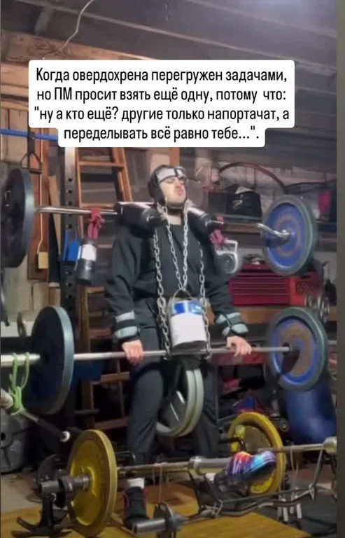 A man in a black tracksuit lifting weights with a bucket on his chest, surrounded by gym equipment.