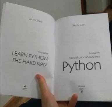 A hand holding an open book with 'Learn Python the Hard Way' in English and Russian