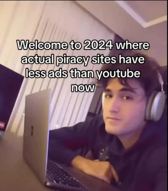 a man wearing headphones sits at a laptop with a look of dismay on his face