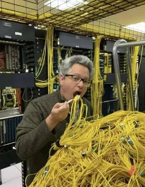 A man in glasses eating a bundle of yellow ethernet cables in a server room with messy racks.