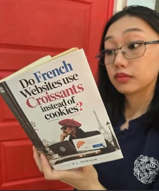 Woman holding a book titled Do French Websites Use Croissants Instead of Cookies