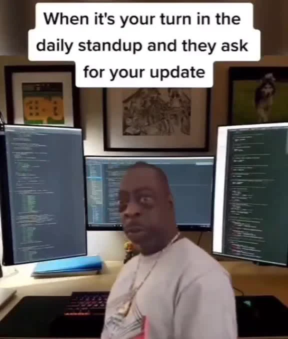 Man sitting at desk with multiple computer monitors looking unprepared for daily standup