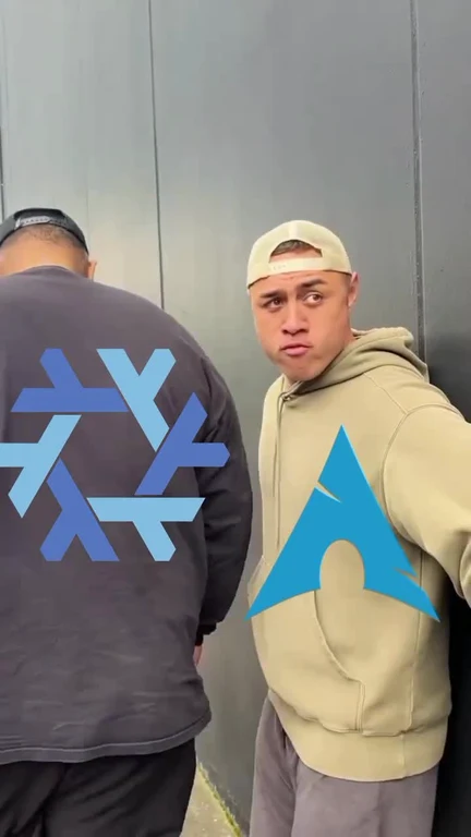 Two men standing against a gray wall with blue logos on their shirts