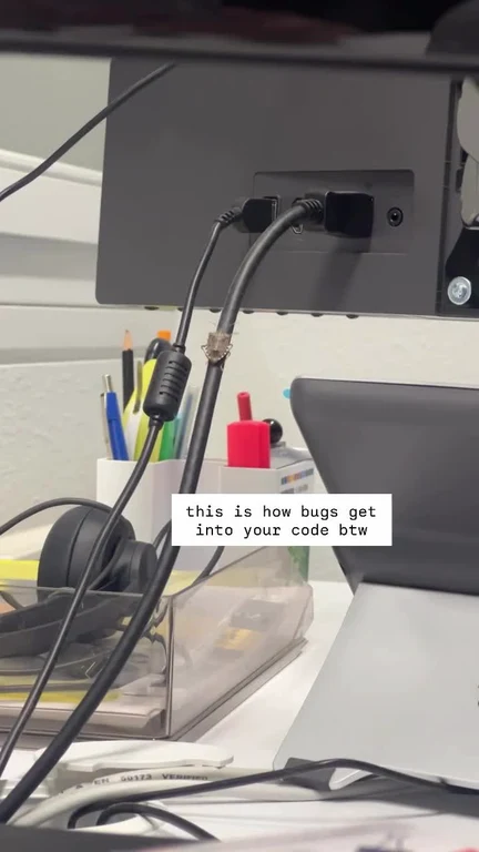 A photo of a messy desk with tangled cables and a caption reading 'this is how bugs get into your code btw'