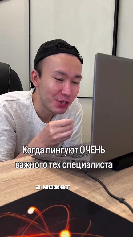man in white shirt and black cap looking at laptop with shocked expression