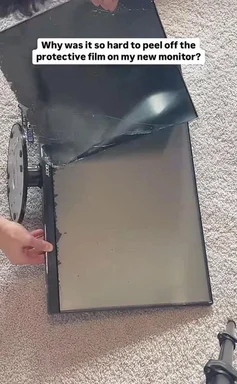A person struggling to peel off the protective film from a new monitor