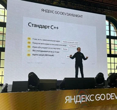 man on stage in front of a projector screen with a humorous list about C++ standards
