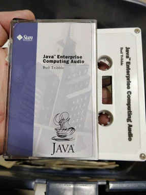A hand holding a cassette tape labeled 'Java Enterprise Computing Audio' by Bud Tribble.