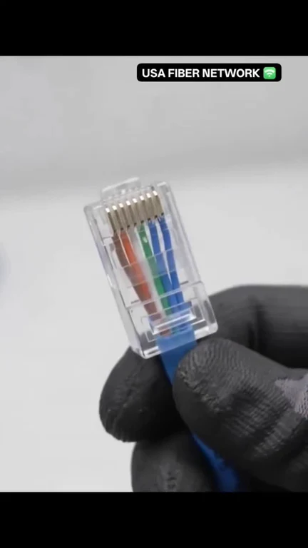 Hand in a black glove holding a clear RJ45 ethernet connector with color-coded wires