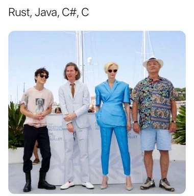 Four people standing in front of a white backdrop with programming languages listed above them