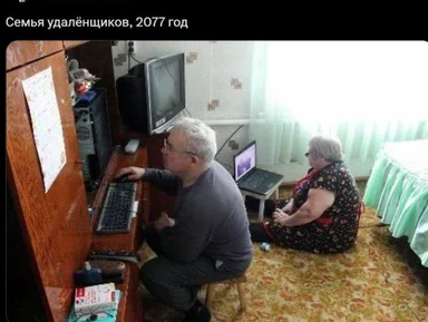 An elderly man and woman sitting at a cluttered desk with multiple computers