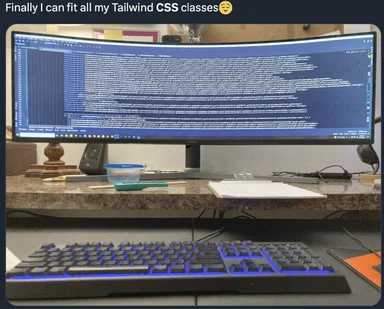 An ultrawide curved monitor displaying one extremely long line of Tailwind CSS classes, with a mechanical keyboard and desk