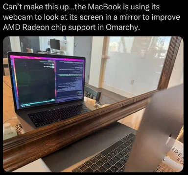 MacBook laptop placed in front of a mirror with code on its screen, satirical image about AI improving AMD Radeon support