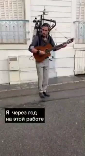 Man walking on a street with a backpack of wires and a guitar strapped to his back, captioned 'Me in a year on this job'