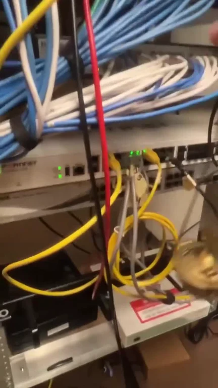 Messy tangled network cables in a server rack with a switch showing green lights.