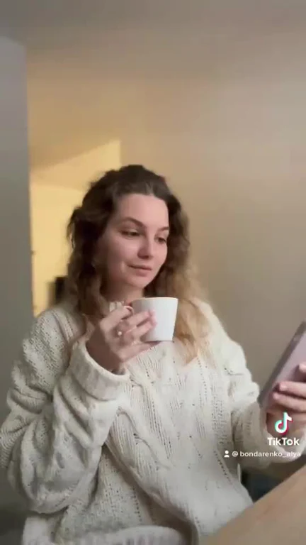woman in white sweater holding cup and phone with tiktok logo