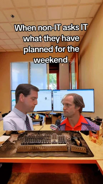 Two men sitting at a desk with a destroyed keyboard, looking at each other