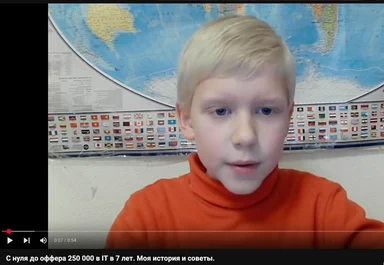 a young boy in an orange turtleneck looks surprised in front of a world map