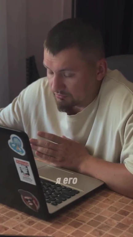 A man looking confused at his laptop with the text 'я его' on the screen.
