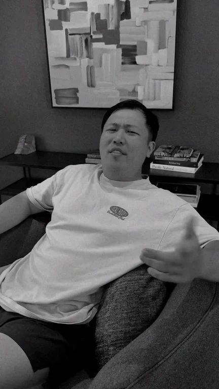 Black and white video of a man sitting on a couch looking sideways with a confused and surprised expression.