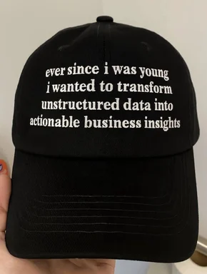 Close-up of a black cap with white embroidered text about transforming unstructured data into actionable business insights.