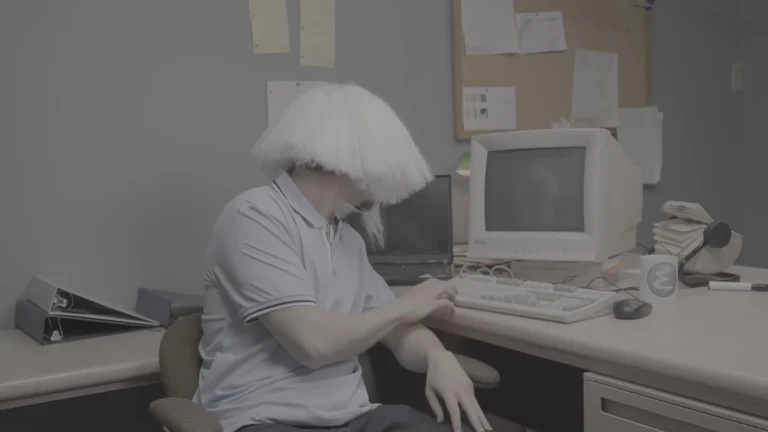 man with puffy white hair sitting at old computer desk