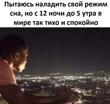 Man looking out over a city at night, contemplating sleep schedule