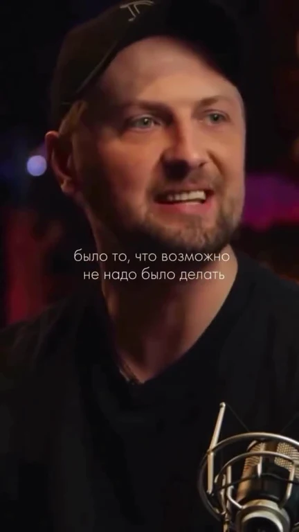 man in black shirt and cap speaking into microphone with russian text overlay