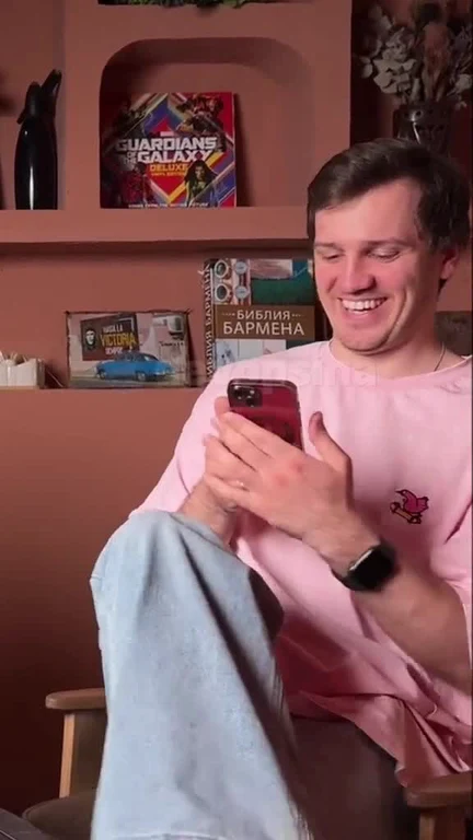 Man in a pink shirt laughing while looking at his phone