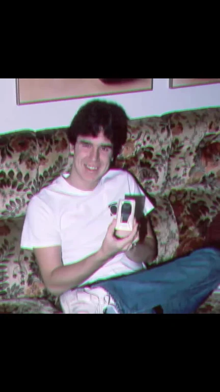 a man sitting on a couch smiling and holding a flip phone