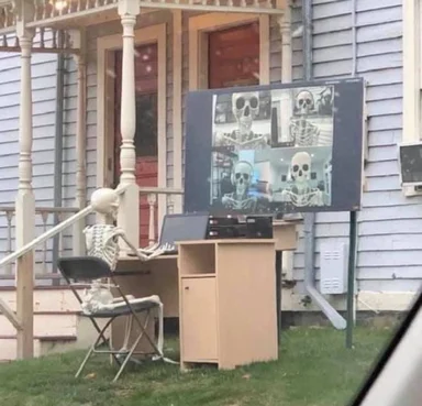 a skeleton sitting at a desk with a laptop and monitor displaying other skeletons on video calls