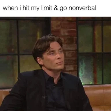Man in a dark suit sitting on a couch with a deadpan, shut-down expression, captioned 'when i hit my limit & go nonverbal'