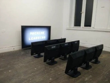 Multiple computer monitors with a TV displaying 'Machine Learning' in the background