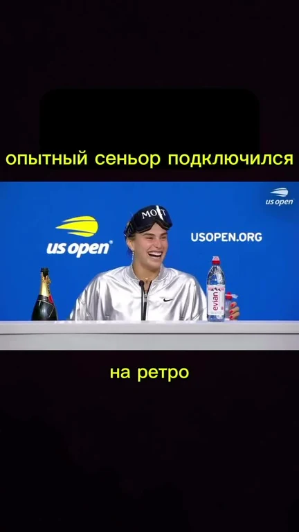 Tennis player in silver jacket laughing with champagne and water bottle on table