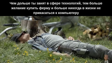 A man in a plaid shirt and cap lies on grass with a VR headset on his legs, a bicycle and woodpile in the background.
