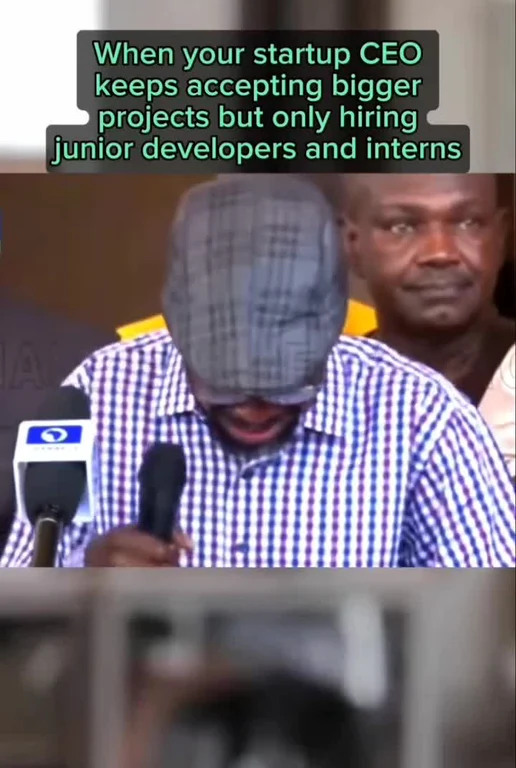 Man with plaid shirt and blurred face speaking into microphones, with another man in the background, text 'When your startup CEO keeps accepting bigger projects but only hiring junior developers and interns'
