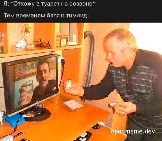 Man in a black shirt with white stripes laughing and holding a mug while looking at a computer screen showing another man
