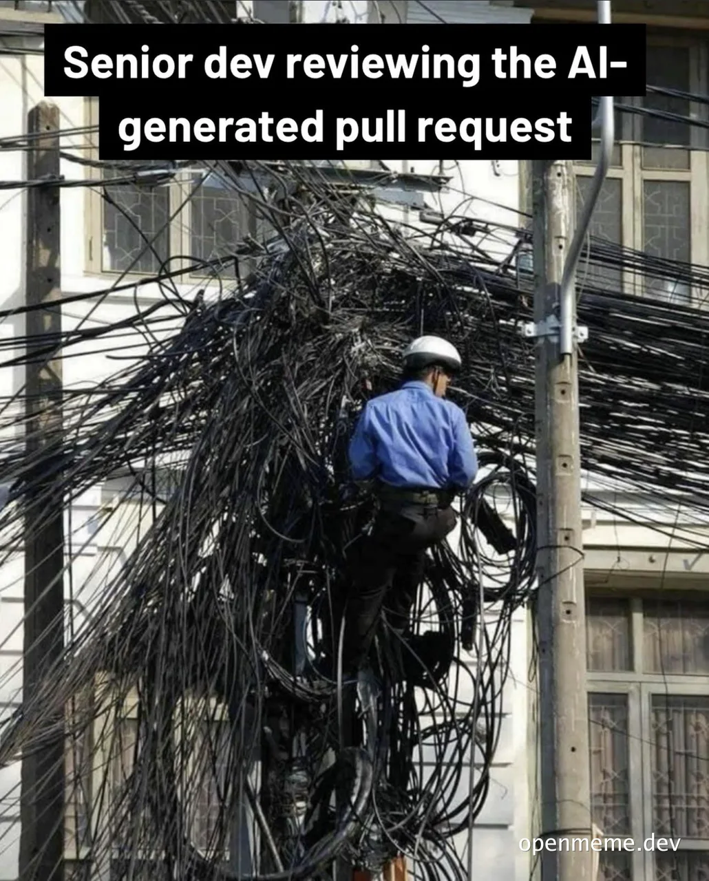 A worker in a blue shirt and white hard hat climbs a utility pole buried under a chaotic tangle of black cables, captioned