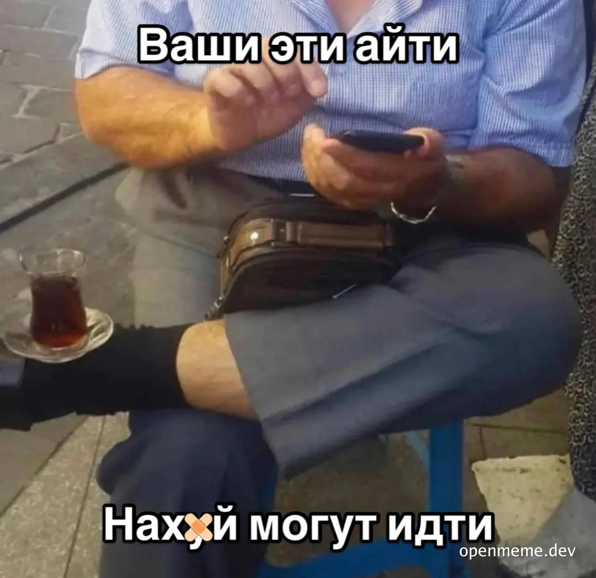 Man sitting on a stool with a cup of tea, looking at his phone with a humorous expression, related to IT