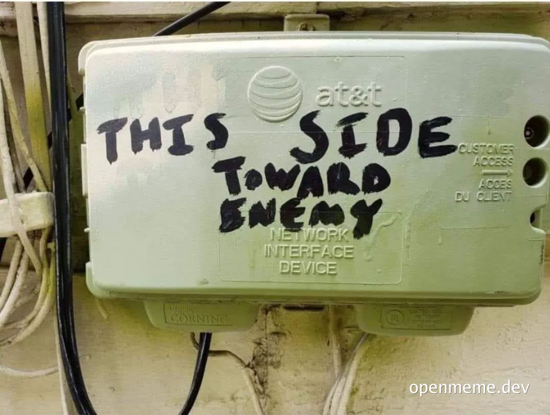 Close-up of a white AT&T Network Interface Device box with black graffiti reading 'THIS SIDE TOWARD ENEMY'
